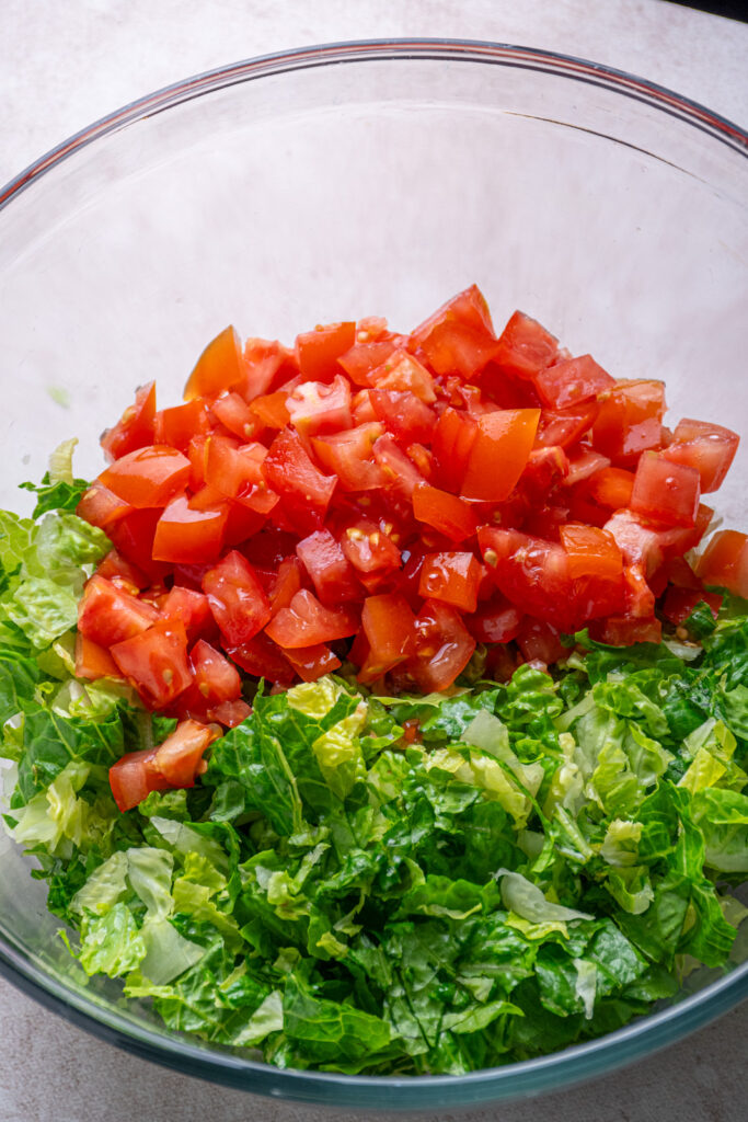 Adding diced tomatoes to the bowl with lettuce.