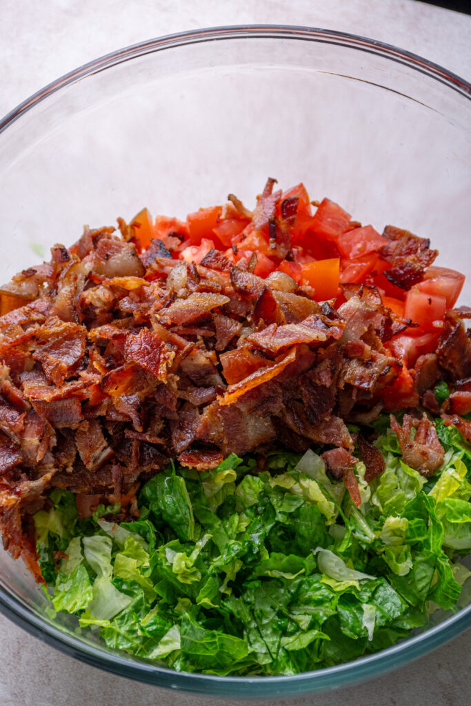 Adding bacon to the bowl with the lettuce and tomatoes.