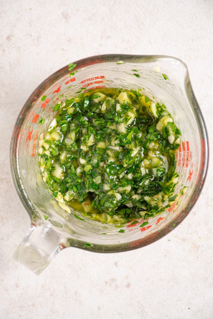 Marinade for jumbo shrimp in a glass measuring cup filled with parsley, garlic, and olive oil.