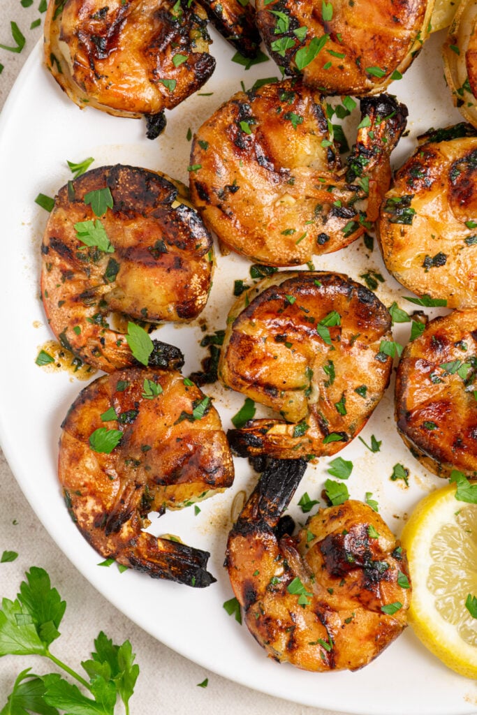 White plate filled with grilled jumbo shrimp garnished with fresh parsley.