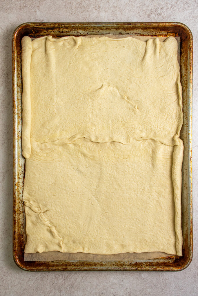 Raw crescent roll dough rolled out on a sheet pan with parchment paper.