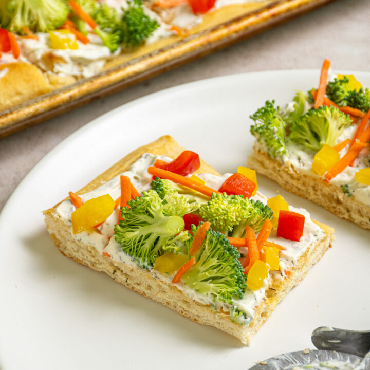 A slice of veggie pizza with broccoli, carrots, and bell pepper on a white plate.