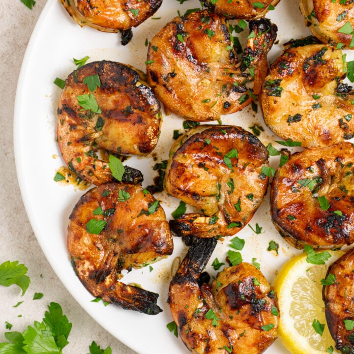 White plate filled with grilled jumbo shrimp garnished with fresh parsley.