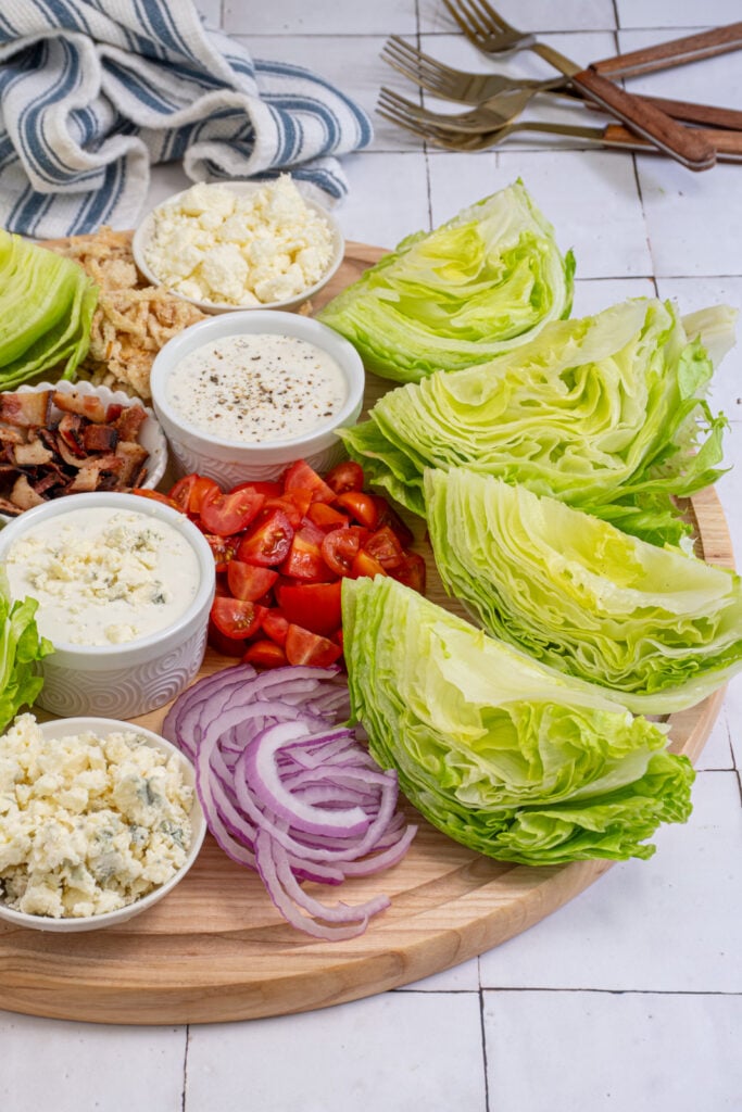 A charcuterie wedge salad board with iceberg lettuce, dressings, and toppings.