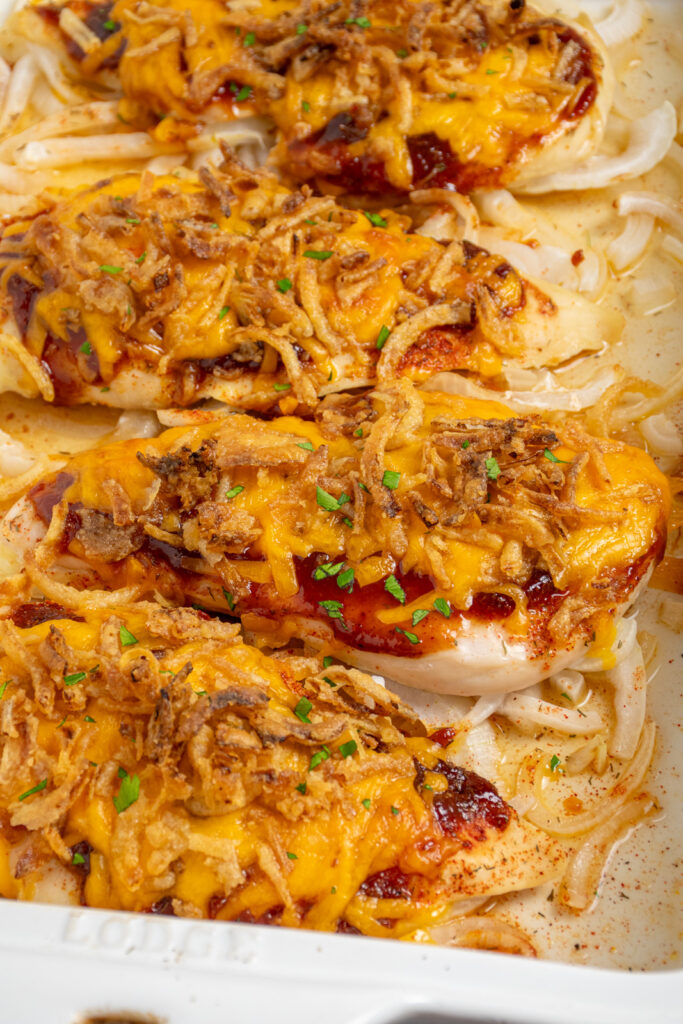 Close up of cheesy bbq chicken breasts in a white casserole dish.