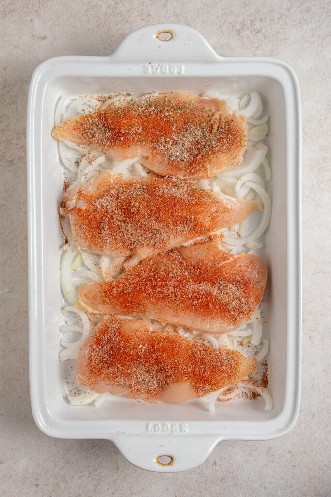 Adding spices to chicken breasts in the casserole dish.