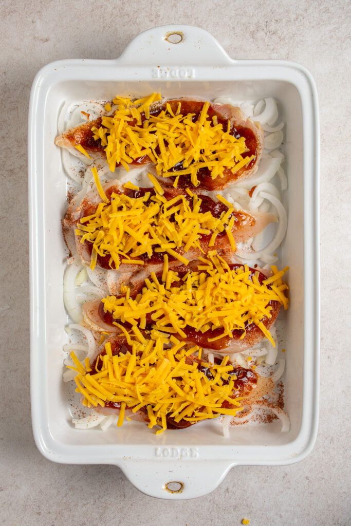 Adding shredded cheddar cheese to chicken breasts in a casserole dish.