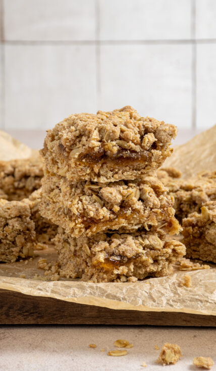 A stack of three fig oat bars showing of the chewy oatmeal crust and crumble topping with fig jam in the middle.