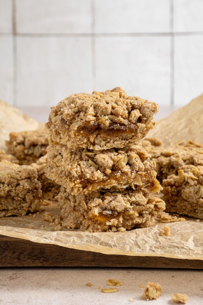 A stack of three fig oat bars showing of the chewy oatmeal crust and crumble topping with fig jam in the middle. 
