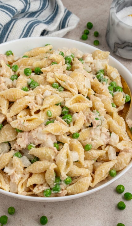 A white serving bowl filled with tuna pasta salad with fresh green peas.