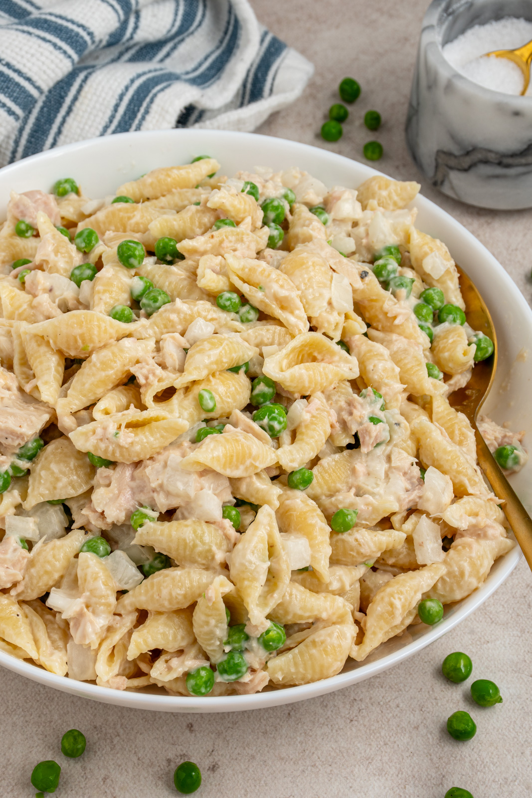 A white serving bowl filled with tuna pasta salad with fresh green peas.
