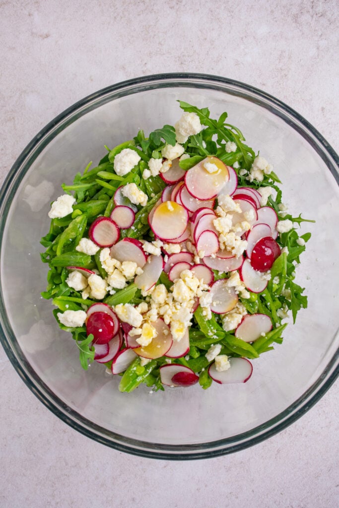 A large mixing bowl with arugula, snap peas, radishes, and feta.