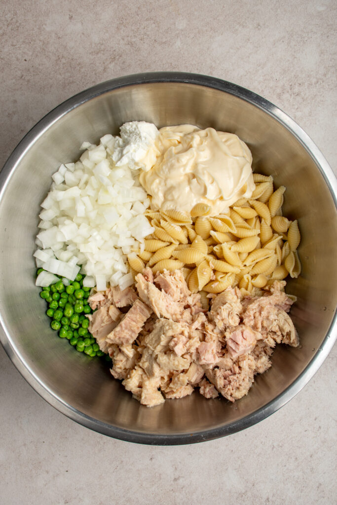 The ingredients to make tuna pasta salad laid out in a large mixing bowl ready to be combined.