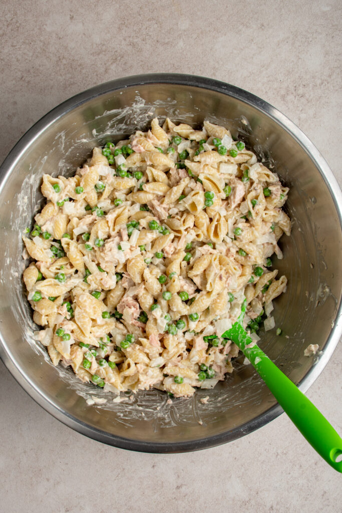 Mixing together the ingredients to make tuna pasta salad in a large stainless steel mixing bowl.