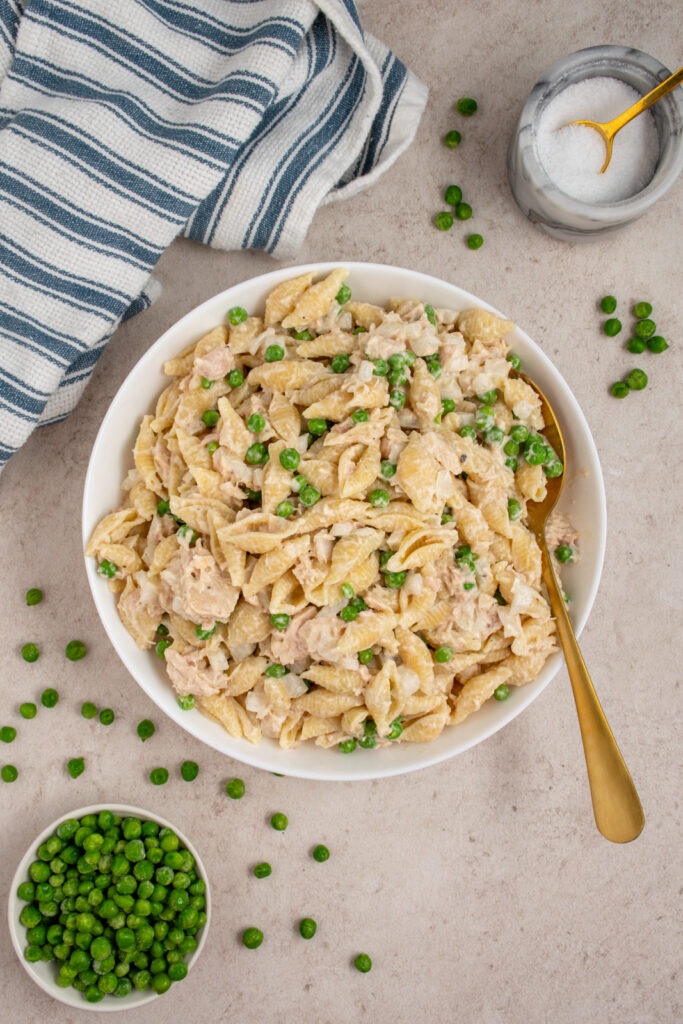 Overhead view of a white bowl filled with cold tuna pasta salad with green peas.