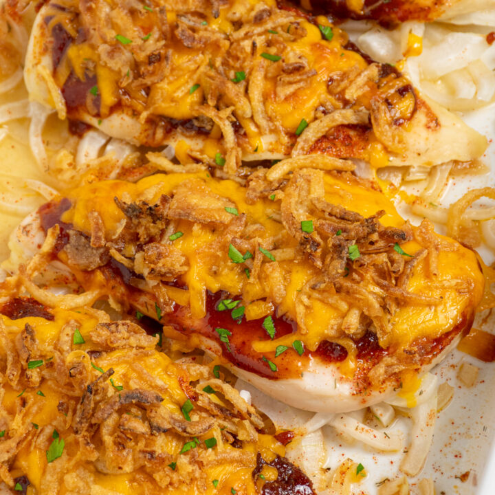 Cheesy bbq chicken breasts in a casserole dish with melted cheese and crispy fried onions.
