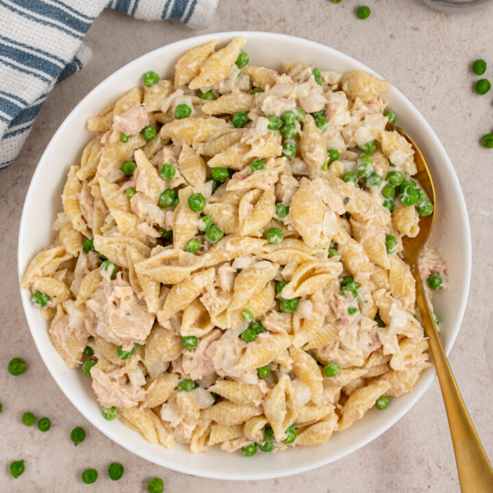 Overhead view of a white serving bowl filled with tuna pasta salad with fresh green peas.