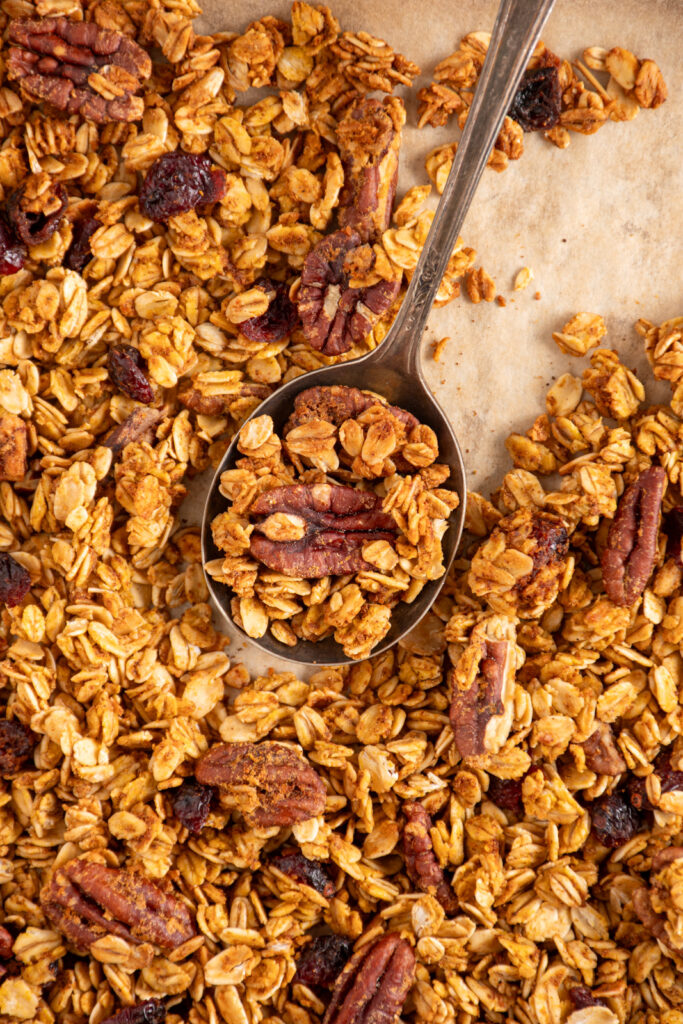 Close up of pumpkin spice granola with dried cranberries and pecans with a spoon scooping some granola.