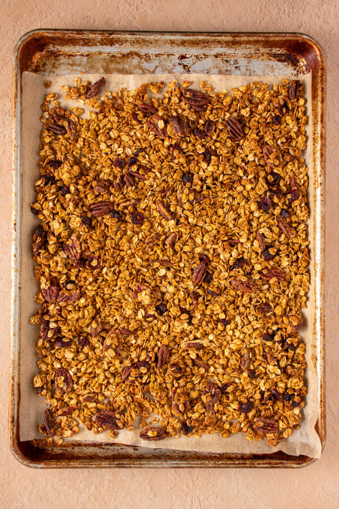 Sheet pan with parchment paper filled with freshly baked pumpkin spice granola with dried cranberries and pecans.