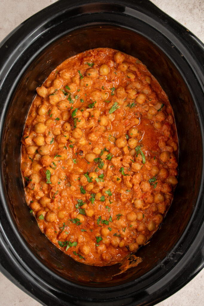 A black crockpot with chickpea tikka masala garnished with fresh cilantro.