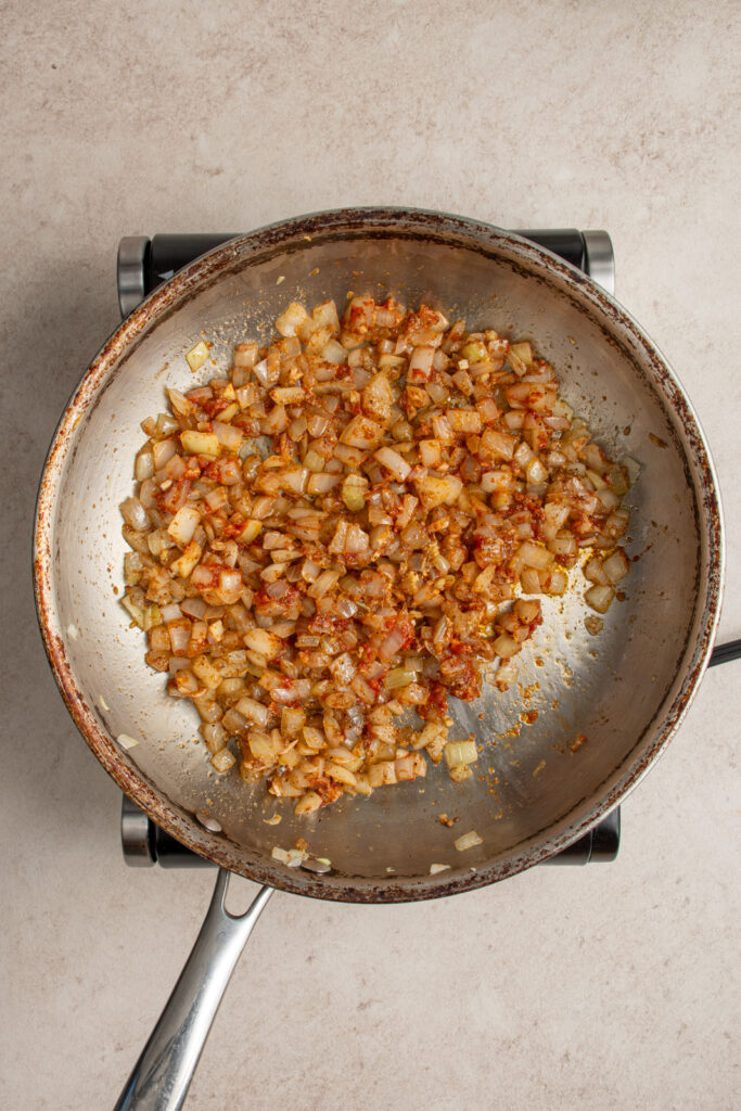 Cooking the tomato paste and spices with the onions in a skillet.