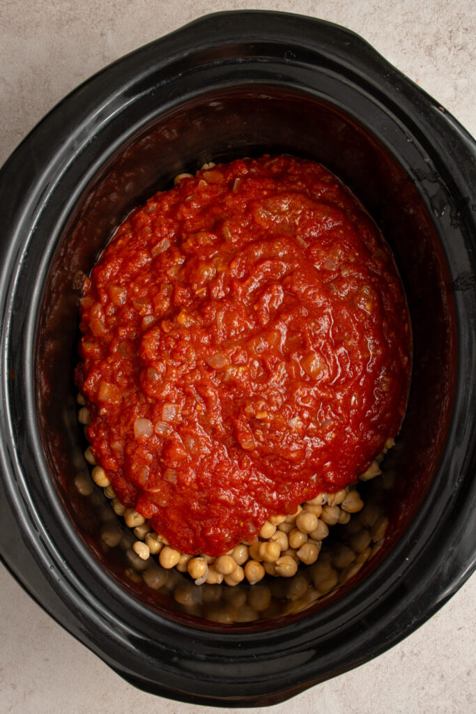 Combining crockpot chickpeas with the spices, onions, and tomatoes.