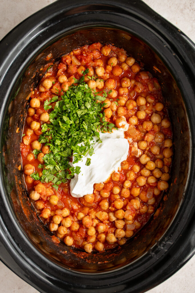 Adding yogurt and cilantro to the crockpot filled with chickpeas.