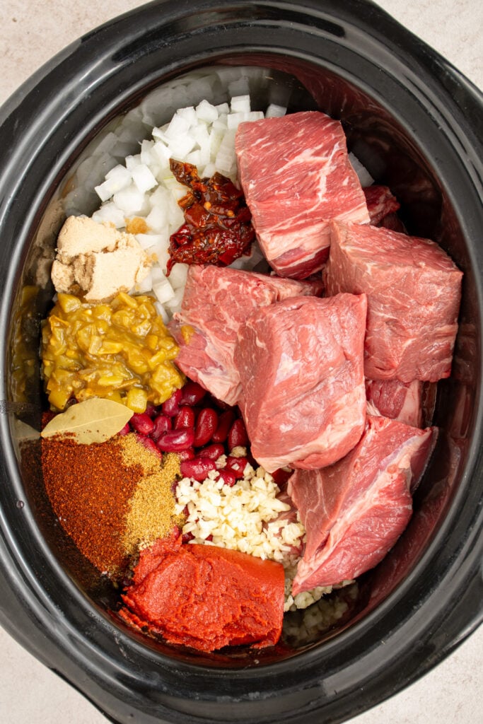 All of the ingredients for making chuck roast chili arranged in the crockpot before mixing to cook.