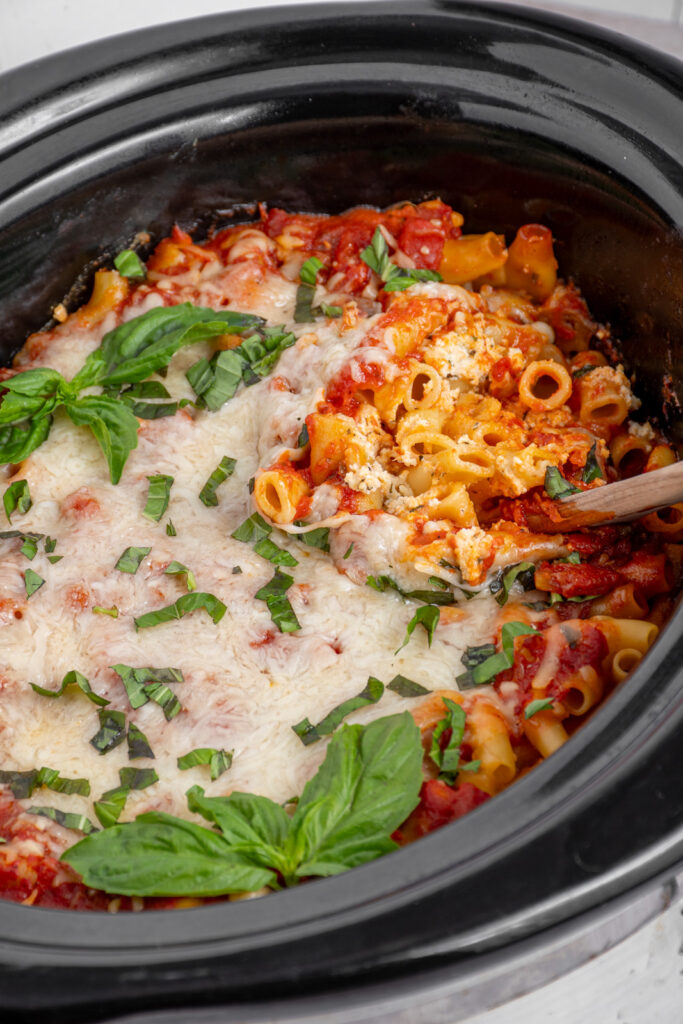 A black crockpot filled with layers of pasta, cheese, and sauce to make crockpot ziti.