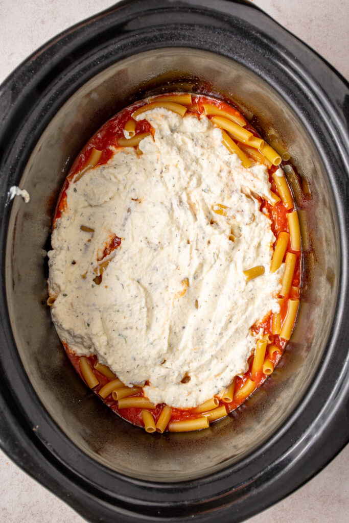 Layering the ricotta cheese in the crockpot overtop sauce and noodles.