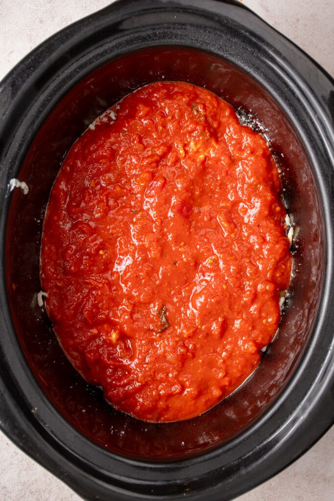 Adding a layer of tomato sauce to a crockpot for ziti.