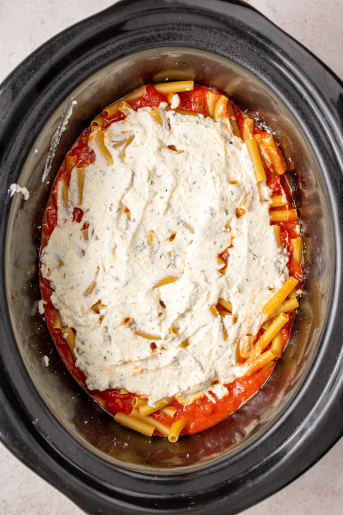 Adding a layer of ricotta to the crockpot.