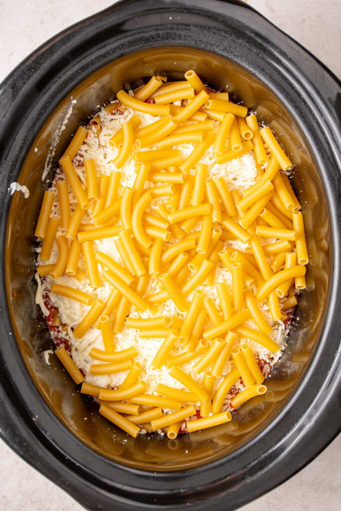 Adding ziti pasta to the crockpot to add a layer to crockpot ziti.