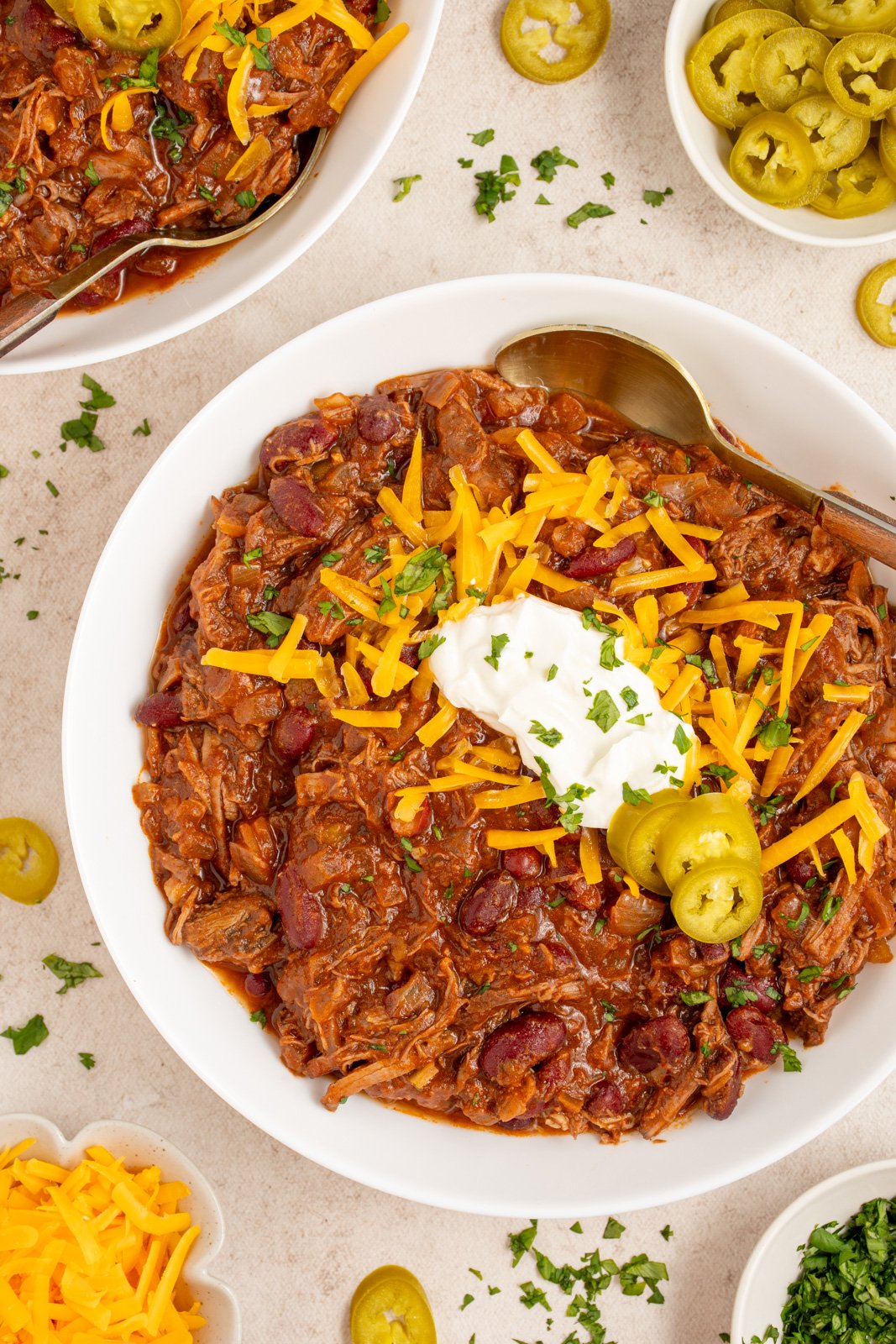 A white bowl filled with chuck roast chili garnished with cheddar cheese, sour cream, and jalapeño slices.