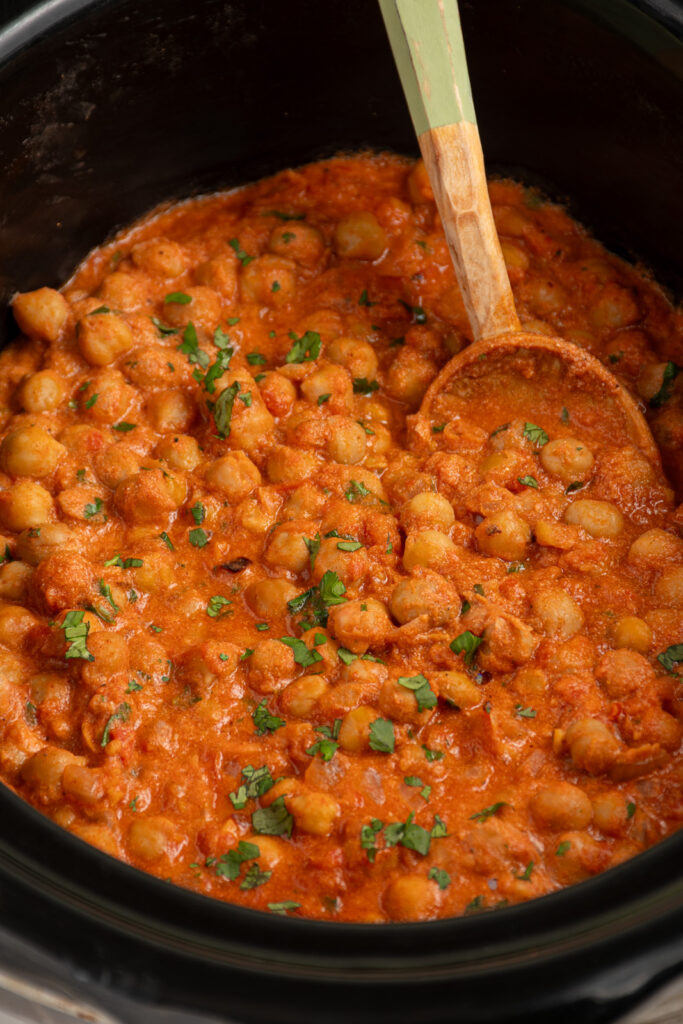 Healthy chickpea tikka masala in a black crockpot with a wooden serving spoon.