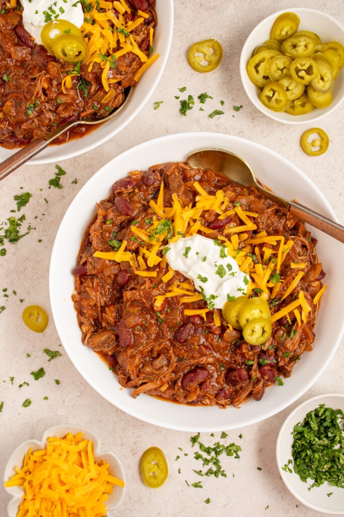 Overhead of a white bowl filled with chick roast chili and garnished with cheddar cheese, sour cream, and jalapeño slices.