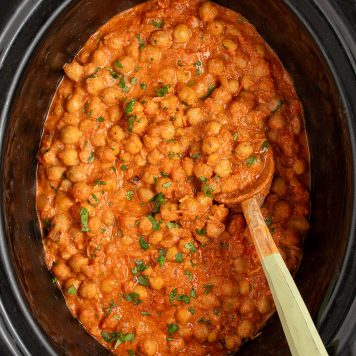 A black crockpot filled with chickpea tikka masala with a wood serving spoon.