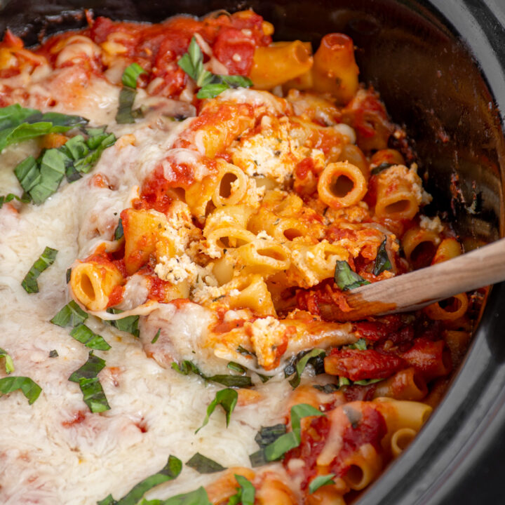 A close up of crockpot ziti with a spoon digging in to show the cooked pasta.