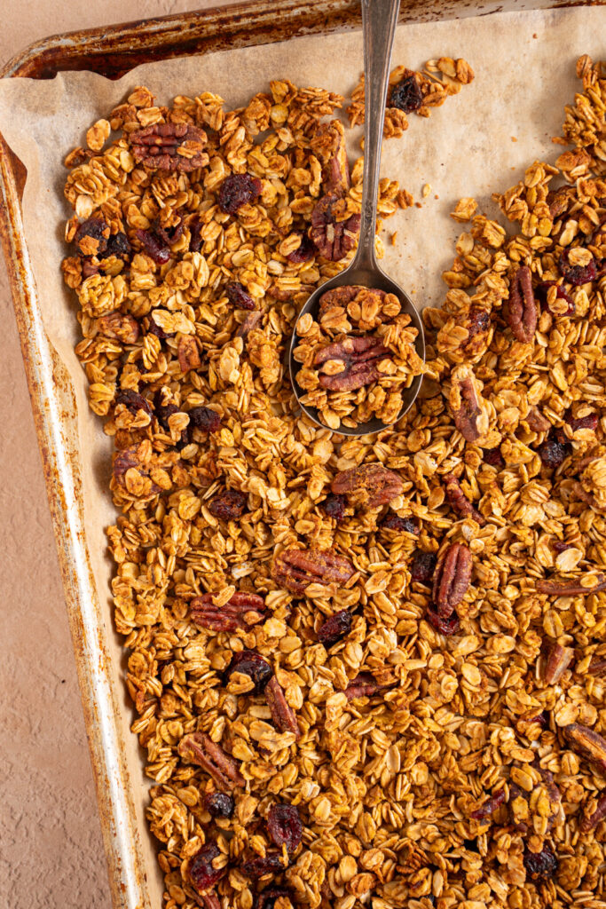 Sheet pan with parchment paper filled with pumpkin spice granola with dried cranberries and pecans.