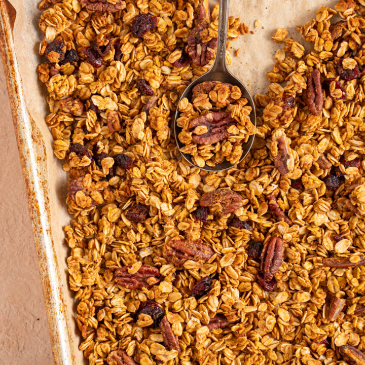 Sheet pan with parchment paper filled with pumpkin spice granola with dried cranberries and pecans.