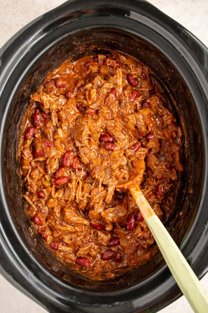 A large wood spoon in the crockpot holding chuck roast chili.