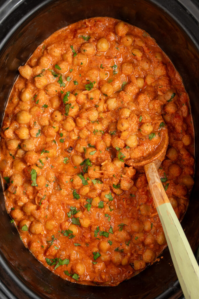 A serving spoon in a black crockpot filled with chickpea tikka masala.