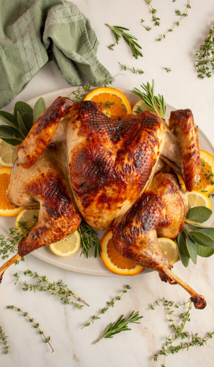 A roast spatchcock turkey on a platter with fresh herbs and citrus.