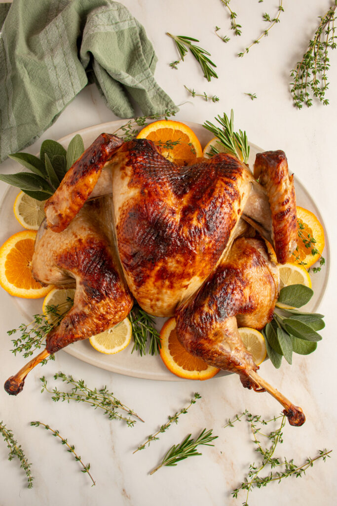 A roast spatchcock turkey on a platter with fresh herbs and citrus.