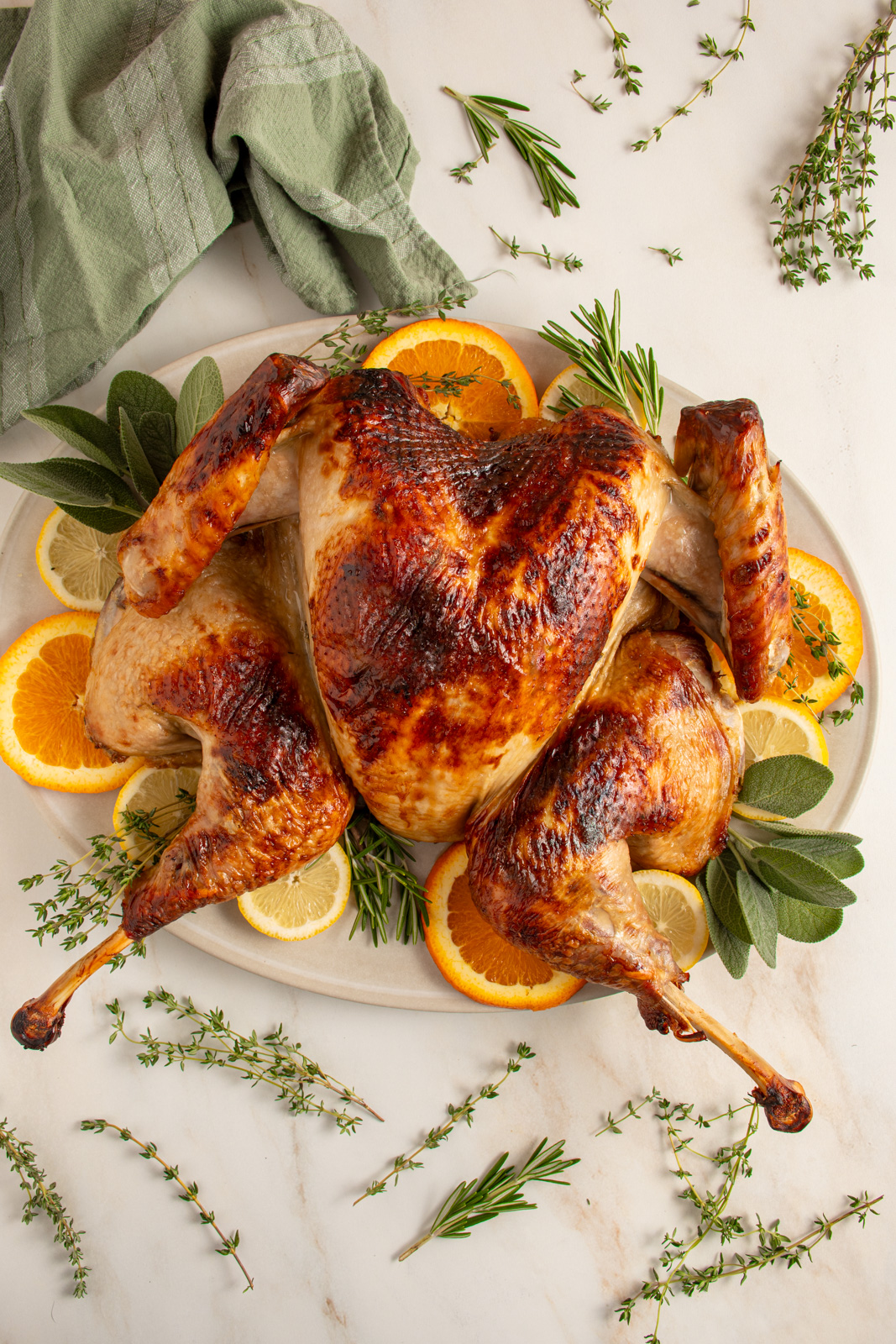 A roast spatchcock turkey on a platter with fresh herbs and citrus.