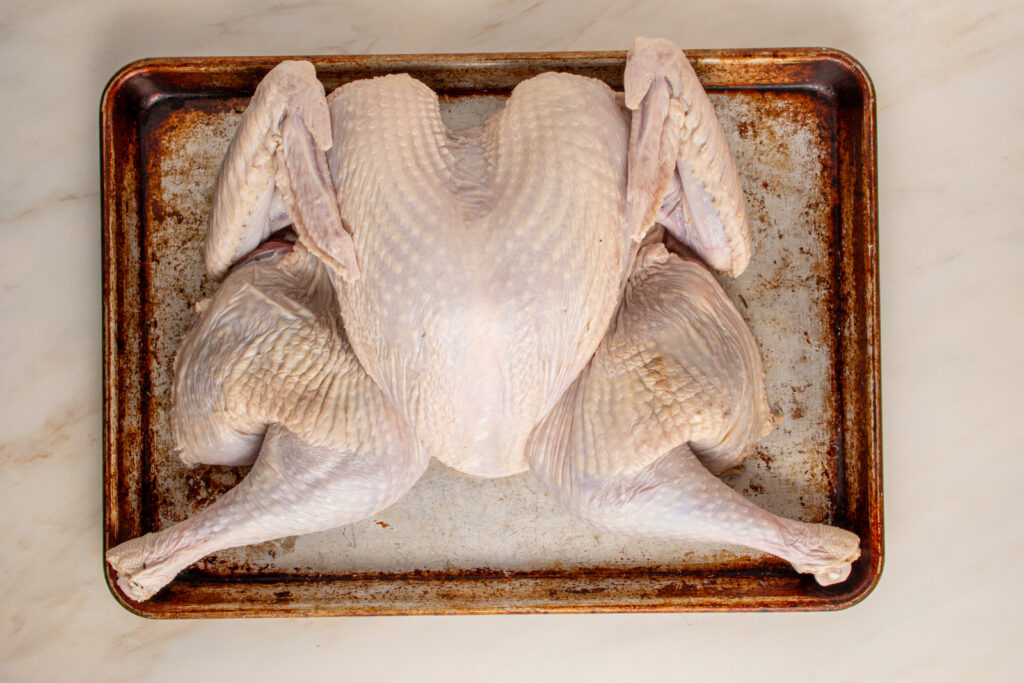 A flat spatchcocked turkey laying on a sheet pan.