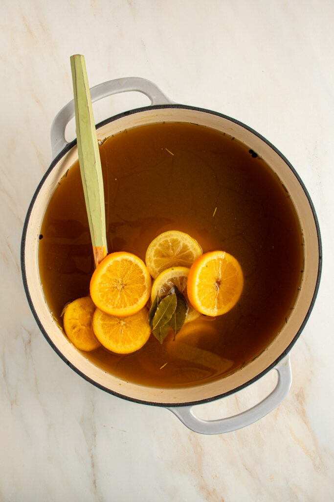 A large pot with apple cider turkey brine with orange slices, lemon slices, bay leaves, and smashed garlic.