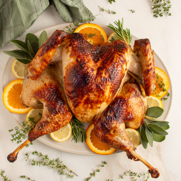 A golden roast spatchcock turkey on a platter with fresh herbs and citrus.