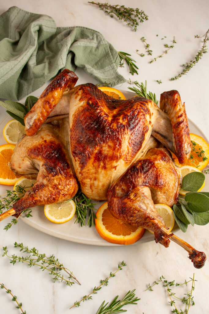 A roasted spatchcocked turkey on a platter with fresh herbs and citrus.