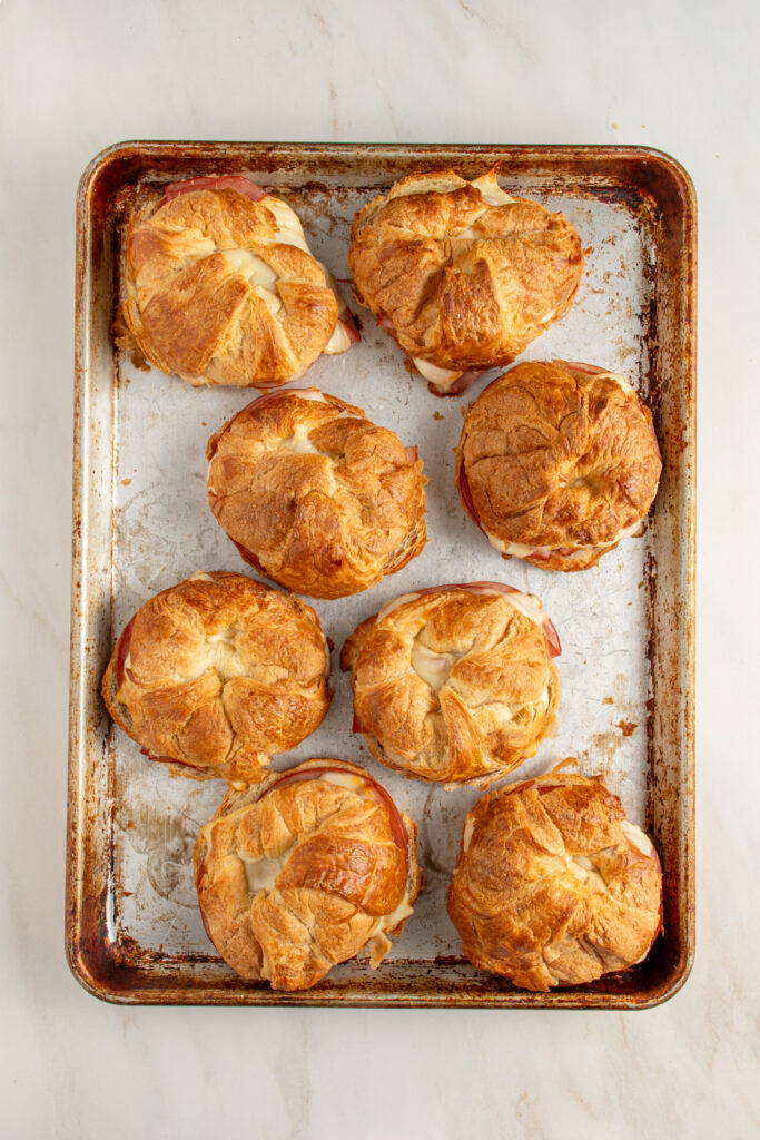 A baking tray full of crispy and flaky baked ham and cheese croissants.